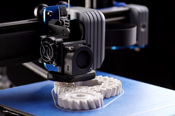 gantry with x-carriage and print head of a FDM-3D-printer that produces white helical gears on blue...