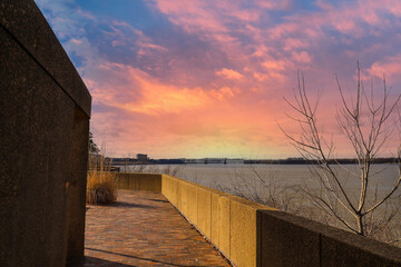 Obraz na płótnie Canvas the Memphis & Arkansas Bridge over the vast flowing waters of the Mississippi river with dry brush along the banks with powerful clouds and yellow sky at Mud Island Park in Memphis Tennessee USA