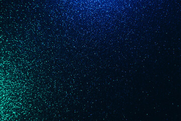 Color glitter overlay. Blur sparkles. Bokeh light. Night sky stars reflection. Neon blue green grain texture glow on dark black shimmering abstract background.