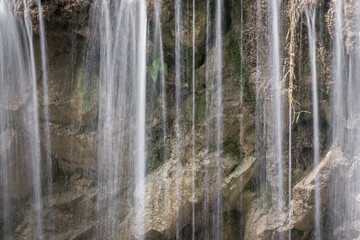 Scenic, close-up view of water cascade of a waterfall, splashing down the wet, yellow, vertical cliff