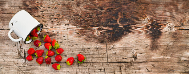 Strawberries sprinkled from a mug on a wooden background.