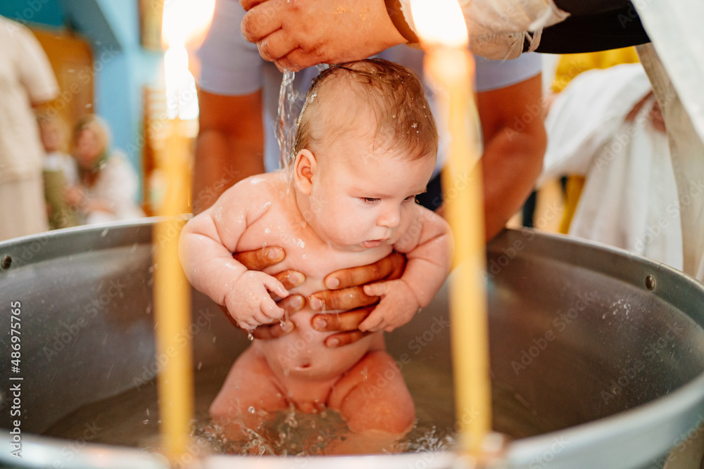 Wall mural the baby boy is lowered into a font with holy water at baptism in the church. 