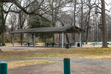 a wooden pergola near a still green lake with green metal park benches underneath surrounded by...