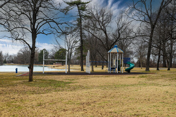 a white and blue jungle gym and a swing set in the park surrounded by yellow winter grass and bare...