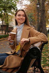 Beautiful young woman wearing stylish clothes with cup of coffee in autumn park