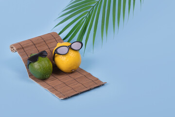 Creative fun idea with a lemon and lime in sunglasses lying on a sun bed on a bright blue...