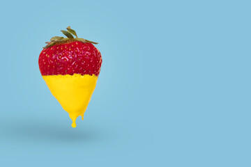 Minimal concept made with strawberry dripping with yellow paint on bright blue background.