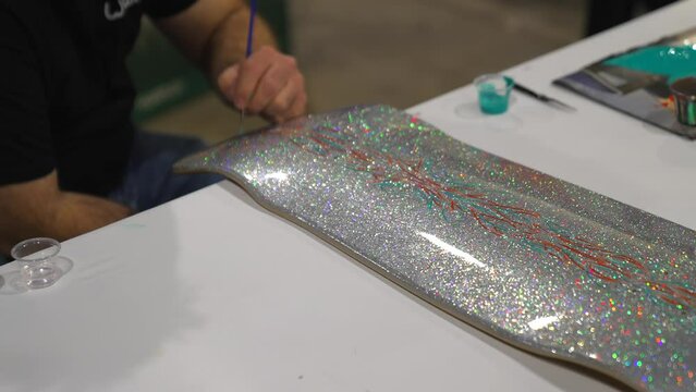 This video shows the hand of an artist pin-striping and drawing on a metallic skate board.