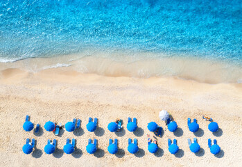 Fototapeta na wymiar Aerial view of blue sea, sandy beach with sun beds and umbrellas at sunset in summer. Tropical landscape with turquoise water, people, deck chair. Travel and vacation. Lefkada island, Greece. Top view