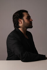 Side-view of bearded man in black suit sitting over white background. Vertical.