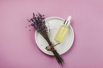 Lavender bouquet  on a plate and a bottle of essential oil on a pink background.Natural organic cosmetics.Place for text.