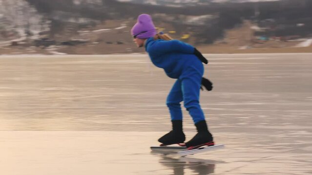 The girl train on ice speed skating. The child skates in the winter in blue sportswear suit, sport glasses. Children speed skating sport. Outdoor slow motion. Snow capped mountains, beautiful ice.