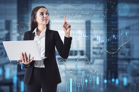 Attractive happy european businesswoman using laptop with abstract glowing big data forex candlestick chart on blurry office interior background. Toned image. 