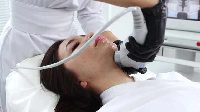 Body massage - young brunette woman having an electric massage procedure on her face - working under her chin