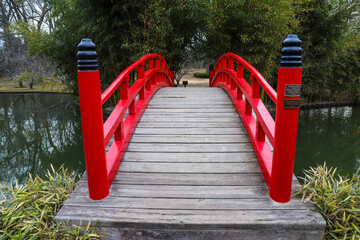 an arched red and black bridge over a lake surrounded by lush green plants and trees in a Japanese...
