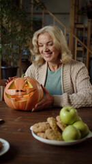 An elderly lady is holding a pumpkin and looking to the camera