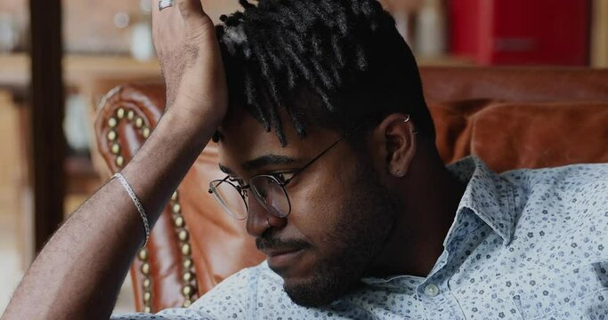 Close up view thoughtful doubtful African hipster man prop head with hand lost in thoughts hesitate ponder on important decision choice. Pensive young guy contemplate on work life problem feel unsure