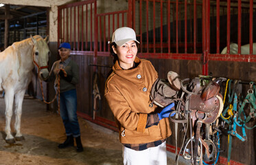 Asian woman rancher carrying horse tack and saddle in horse farm.