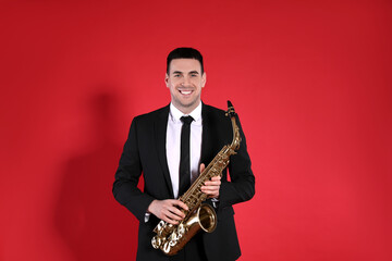 Fototapeta premium Young man in elegant suit with saxophone on red background