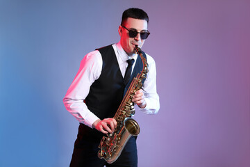 Fototapeta na wymiar Young man in elegant outfit playing saxophone on color background