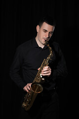 Fototapeta na wymiar Young man playing saxophone on dark background