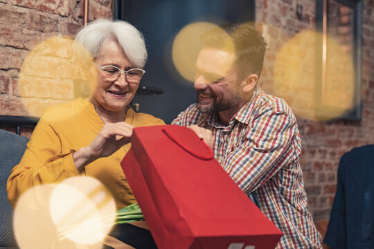 grandmother receiving a gift in a red bag for grandma's day from her adult grandchild man. High quality photo