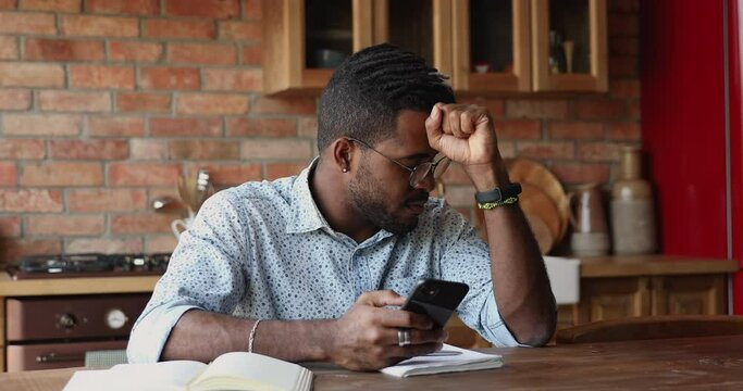 Annoyed angry millennial Black male hipster hold mobile phone feel outraged by low wifi internet signal bad connection application crash. Concerned worried young guy deal with software problem on cell