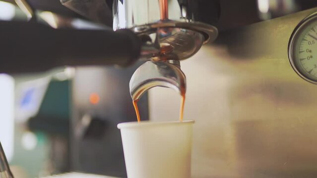 4k, espresso coffee is pouring from the coffee machine into a white paper cup, slow motion
