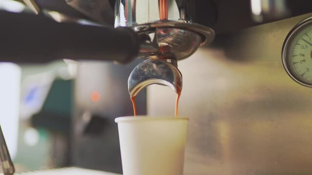 4k, espresso coffee is pouring from the coffee machine into a white paper cup, slow motion