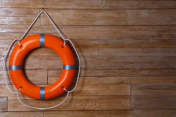 Orange lifebuoy on wooden background, space for text. Rescue equipment