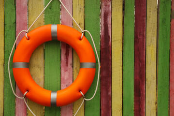 Orange lifebuoy hanging on color wooden fence, space for text. Rescue equipment
