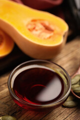 Glass bowl of pumpkin oil and seeds on wooden table, closeup