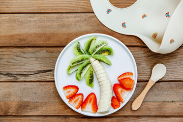Creative meal for a child, strawberries and banana, funny food over wooden background. Fruits for baby. Top view, flat lay