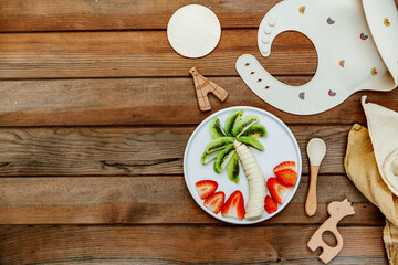 Creative meal for a child, strawberries and banana, funny food over wooden background. Fruits for baby. Top view, flat lay