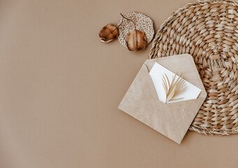 Straw stand, envelope and card, dry flowers on neutral beige background. Aesthetic minimal background. Flat lay, top view.