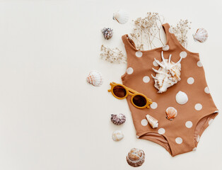 Little girl's cute swimsuit with sunglasses and seashells on beige background. Retro fashion baby, summer holidays concept