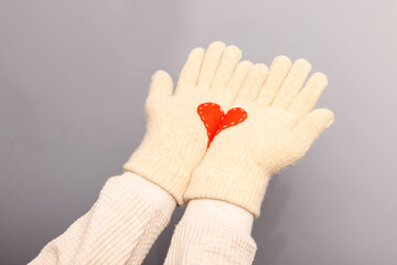 Women hands in white knitted gloves with red heart