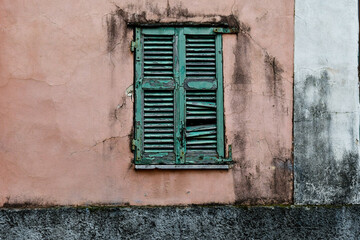 Close-up of the closed window of an old house with weathered, damaged shutters on a pink, dirty wall, Sanremo, Imperia, Liguria, Italy