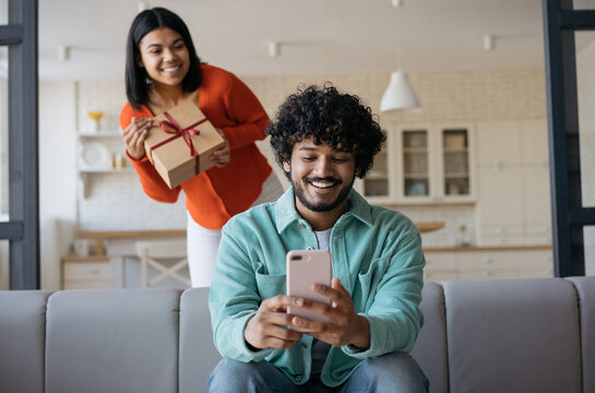 Beautiful African American Woman Holding Gift Box, Prepare Surprise For Boyfriend. Birthday Present Concept. Handsome Smiling Indian Man Using Mobile Phone Shopping Online, Ordering On Website  