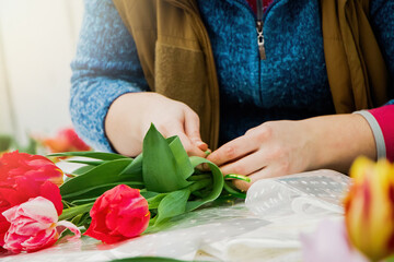 Woman florist makes bouquet of fresh tulips. Spring flowers in flower shop.