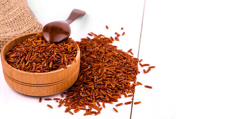 Dark rice, burlap and spoon in a wooden cup on a white dining table.