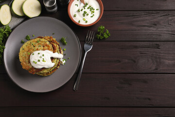 Delicious zucchini fritters with sour cream on wooden table, flat lay. Space for text
