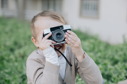 Little happy boy hold film analogue vintage retro photo camera, small photographer look at viewfinder