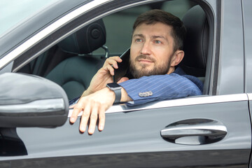 Successful business man with a phone in his hand sits behind the wheel of a prestigious car