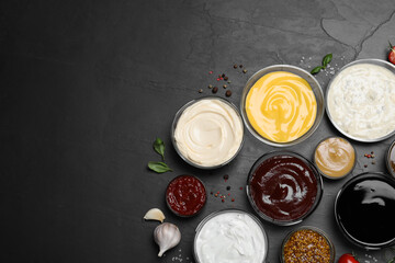 Many different sauces on black table, flat lay. Space for text