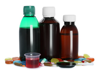 Bottles of cough syrup, dosing spoon, measuring cup and pills on white background