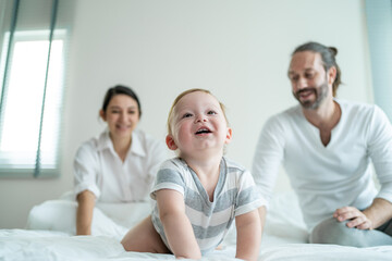 Obraz premium Caucasian parents playing with cute baby boy child on bed in bedroom. 