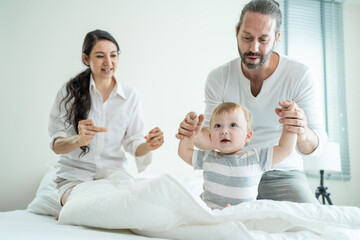 Caucasian loving parents play with baby boy child on bed in bedroom. 