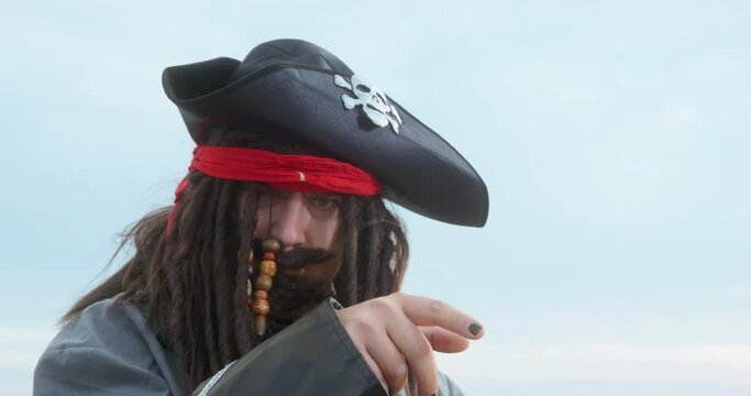 Crazy pirate captain in cocked hat with skull and crossbones and long braids rubs palms to fight ON beach near sea close view