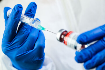 Hands in blue protective glove holding syringe,taking an injection shot from vial ampoule